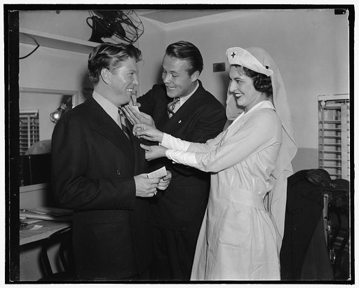 Picture stars enroll in Red Cross. Between appearances at the Earle Theater Johnny Davis, (left) and Wayne Morris receive their Red Cross pins from Miss Carolyn Chantry, Daughter of Capt. Allan Chantry USN and Mrs. Chantry, 9/28/38