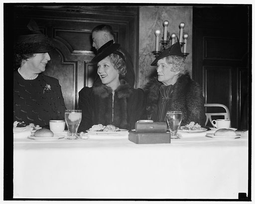 Mary Pickford breaks bread with cab wives at newspaper women's luncheon. Washington, D.C., Nov. 15. Mrs. Cordell Hull and Mrs. Claude A. Swanson, right, wife of Secretary of the Navy, engage in a bit of r[...] with Mary Pickford as they were honor guests [...] the former movie star, at Women's Natio