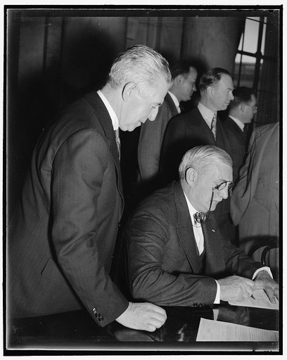 GMC Head signs on the dotted line. Washington, D.C., Dec. 6. William S. Knudsen, President of the General Motors Corp., signs a subpoena before appearing before the Monopoly Committee. George C. Arvedson, Counsel for the Automobile Manufacturers Association, looks on