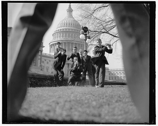 Baseball game with group of men and young boys (pages?) seen through legs of pitcher, with U.S. Capitol in background, Washington, D.C.