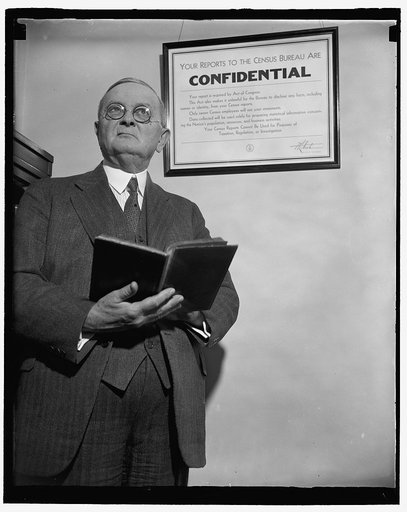 Man holding book, standing in front of sign "Your reports to the Census Bureau are confidential" at the US Census Bureau