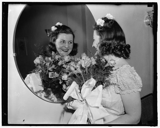 Miss Rose Colliflower holding a bouquet of roses looking at her reflection in a mirror