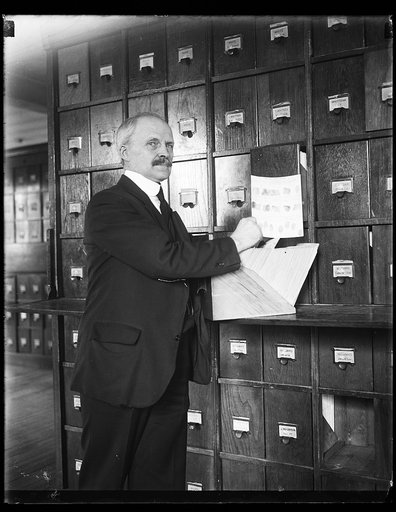 Man holding a sheet of fingerprints labeled "personal identification, right hand" in front of a wood file cabinet