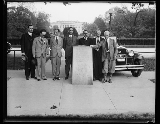 Group standing near marker for measuring distance to Washington, D.C.; White House in background