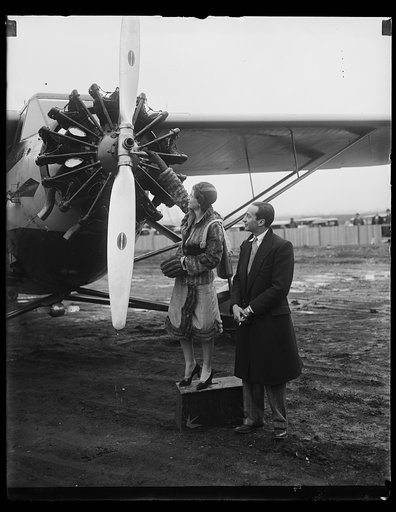 CHRISTENING OF ROUMANIAN PRINCE'S PLANE. Prince Jean Ghica, of Roumania, is watching Miss Betty Powell, daughter of Col. And Mrs. E. Alexander Powell, christen his cabin plane "King Carol II" at Washington-Hoover Airport to-day. The royal pilot hopped off for New York after the ceremony and will lat
