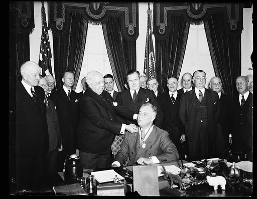 PAN AMERICA SOCIETY HEAD GIVES MEDAL TO ROOSEVELT. JOHN L. MERRILL, PRESIDENT OF THE PAN AMERICAN SOCIETY, PLACES THE SOCIETY'S AWARD ABOUT THE NECK OF PRESIDENT ROOSEVELT. SPRUILLE BRANDEN, MEMBER OF THE SOCIETY'S COUNCIL, IS DIRECTLY BEHIND THE PRESIDENT. THE AWARD WAS FOR ROOSEVELT'S POLICY PROMO