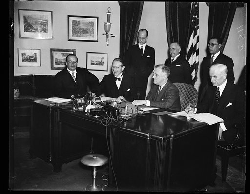 NEW BRAZILIAN TRADE PACT SIGNED. SECRETARY OF STATE CORDELL HULL, RIGHT, SIGNS THE NEW TRADE AGREEMENT BETWEEN THE UNITED STATES AND BRAZIL CALLING FOR RECIPROCAL TARIFF CONCESSIONS. THE PACT WAS SIGNED IN THE PRESIDENT'S OFFICE IN THE EXECUTIVE WING OF THE WHITE HOUSE. OTHERS IN THE PICTURE, FROM T