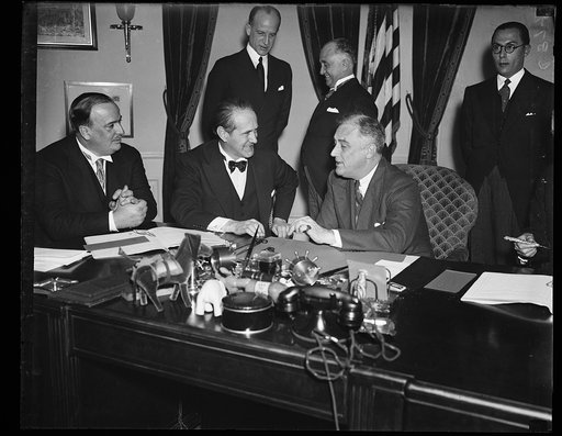 IT'S A DEAL. BRAZILIAN MINISTER OF FINANCE ARTHUR SOUZA COSTA, LEFT, RUBS HIS HANDS TOGETHER, APPARENTLY IN SATISFACTION, AS HE MEETS WITH PRESIDENT ROOSEVELT AT THE SIGNING OF A NEW TRADE PACT BETWEEN HIS COUNTRY AND THE UNITED STATES. BRAZILIAN AMBASSADOR OSWALDO ARANHA, CENTER, AND PRESIDENT ROOS
