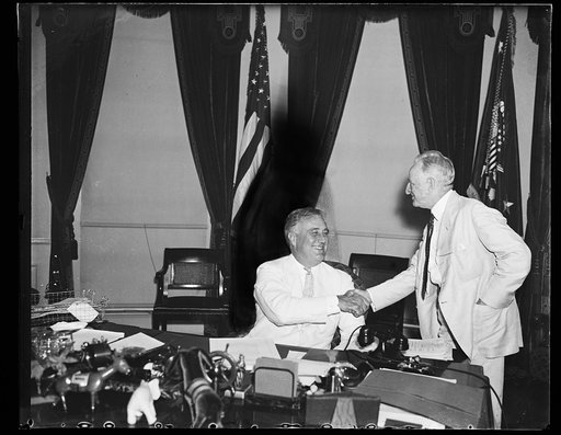 A LITTLE HATCHET BURIAL. PRESIDENT ROOSEVELT, SEATED, GREETS SEN. CARTER GLASS (D-VA) QUITE WARMLY AS SENATORS AND SUCH GATHER AT THE WHITE HOUSE TO WATCH THE PRESIDENT SIGN THE ADMINISTRATION BANKING BILL. SEN. DUNCAN U. FLETCHER (D-FL) STANDS BEHIND PRESIDENT ROOSEVELT. THE LETTERS WERE WRITTEN BY
