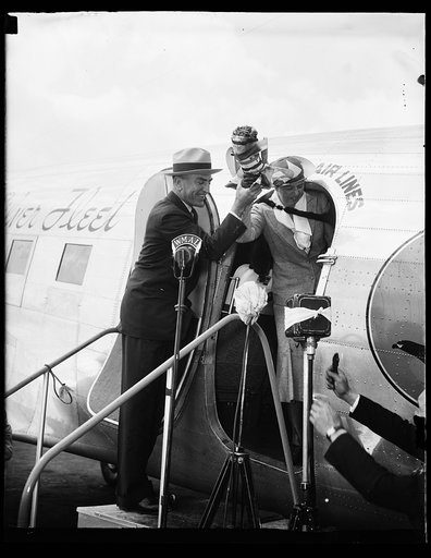 FIRST LADY CHRISTENS PLANE. WASHINGTON, D.C. MAY 17. MRS. FRANKLIN D. ROOSEVELT AND CAPT. EDDIE RICHENBACKER HOLDING THE BOTTLE OF CHAMPAGNE WHICH THE FIRST LADY USED TODAY IN CHRISTENING THE FLAGSHIP OF THE EASTERN AIR LINES WASHINGTON-NEW YORK RUN. UNDER THE NEW SCHEDULE WHICH STARTED TODAY, IT WI