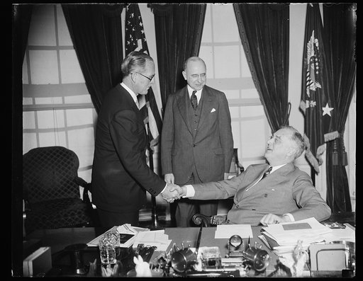 CONGRATULATIONS FROM THE CHIEF. WASHINGTON, D.C. FEBRUARY 18. PRESIDENT ROOSEVELT CONGRATULATES JOSEPH P. KENNEDY, FORMER MARITIME HEAD AND CLOSE ADVISOR OF THE CHIEF EXECUTIVE, SHORTLY AFTER HE TOOK THE OATH AS U.S. ENVOY TO GREAT BRITAIN TODAY IN THE WHITE HOUSE. ASSOCIATE JUSTICE STANLEY REED (CE
