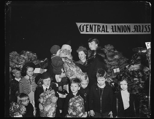FIRST LADY HELPS SANTA. WASHINGTON, D.C. DECEMBER 24. SANTA HAD A HELPER IN MRS. ROOSEVELT AT THE CENTRAL UNION MISSION'S PARTY WHICH TOOK PLACE AT THE LOWE'S CAPITOL THEATER THIS MORNING. L TO R: MRS. ROOSEVELT, MRS. JOHN BENNETT OF THE CENTRAL UNION MISSION, AND HOMER RODEHEAVER AS SANTA