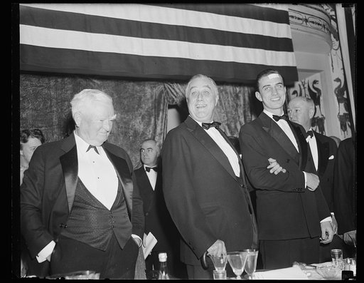 V.P. PENSIVE AS PRESIDENT IS HAPPY OVER RECEPTION AT JACKSON DAY DINNER. WASHINGTON, D.C. JANUARY 8. VICE PRESIDENT GARNER SEEMED PENSIVE IN THIS PICTURE AS PRESIDENT ROOSEVELT ACKNOWLEDGES WITH A SMILE THE TUMULTUOUS GREETING EXTENDED HIM ON ARRIVAL AT THE $100 A PLATE JACKSON DAY DINNER IN WASHING
