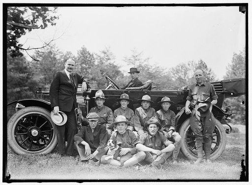 Group of Boy Scouts posed with dog and three men in front of an automobile