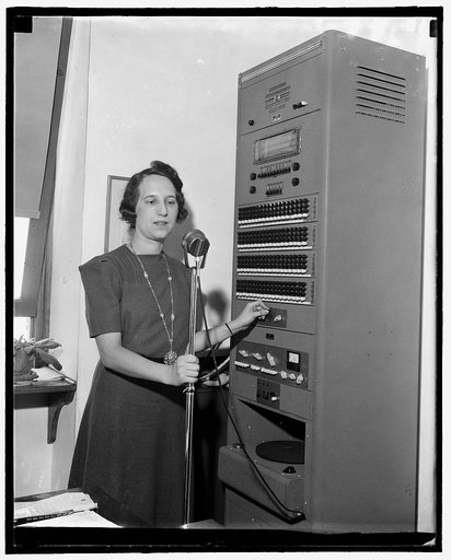 Woman at microphone stand adjusting levers on a large console with Triplett Meter Company decibel display