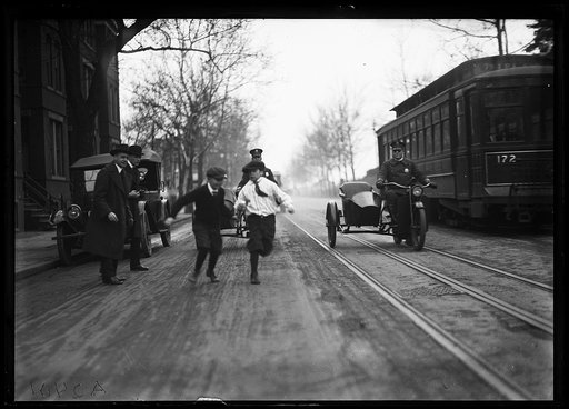 Children, motorcycles with side cars, and streetcar in street