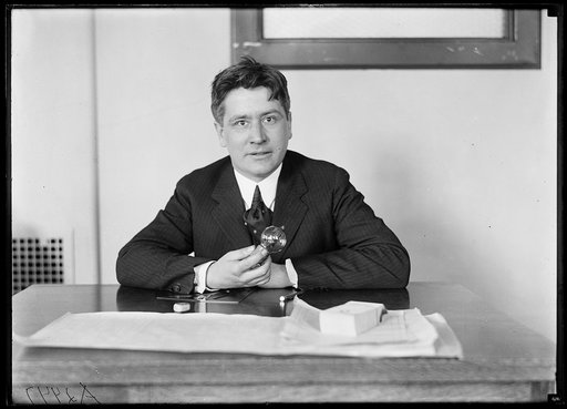 Man seated at desk holding vacuum tube with text: “Property of American Tel. & Tel. Company”