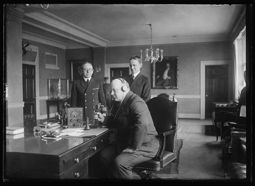 Secy. of Navy Denby "listening in" on his wireless phone recently installed in his office at the new Navy bldg.