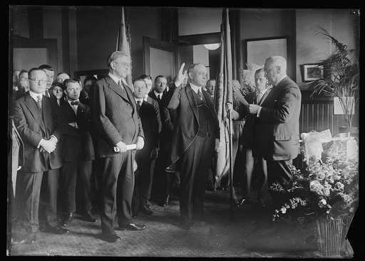 John H. Bartlett being sworn in as Frist Asst. Postmaster Gen. He recently resigned his postition and president of [à] the Civil Service Commission. Oath of office was administered by George R. Wales. L to r.: in foreground: Postmaster Gen. Hubert Work, Mr. Bartlett & George Wales
