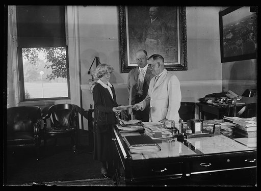 Secy. of Agric. Wallace commissioning Miss Elizabeth U. Hoffman of the office of Home Economics to demonstrate the labor saving methods taught by county home demonstrating agents. C.W. Pugglsey also in photo. (Asst. to the Secy.)