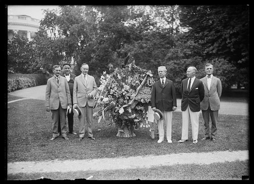 Birthday greetings from the florists of the country were tendered Pres. Coolidge today by the officers and directors of the Florists Telegraph Delivery Assoc. in the form of a Liberty Bell made with flowers. July 4th is the Pres.'s birthday. Lft. to rt.:Wallace McCamant, of Portland, Ore., who nomin
