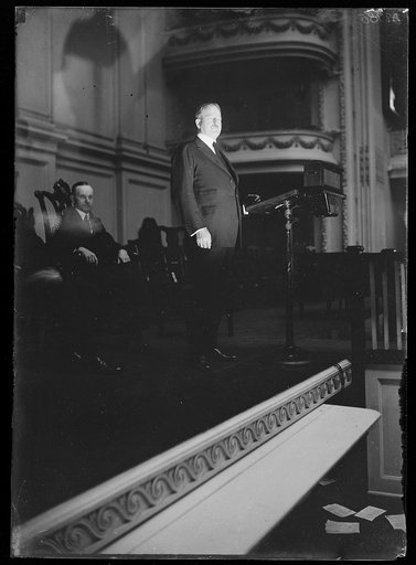 Henry Stimson? at podium on stage with Calvin Coolidge seated in back
