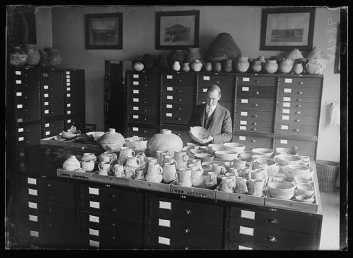 Man examining pottery; "Amer Archeol," i.e., American Archaeology?
