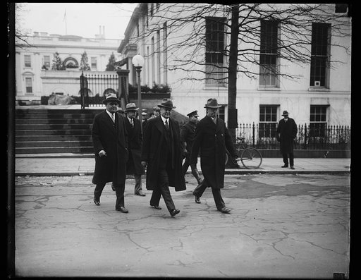 Off for the new offices. President Hoover (center) with Secretary George Akerson, (left) and Secretary Walter Hughes Newton (right). Secret Service men in the background. The picture was made as the President and his Secretaries left the White House for the temporary executive offices in the State, 