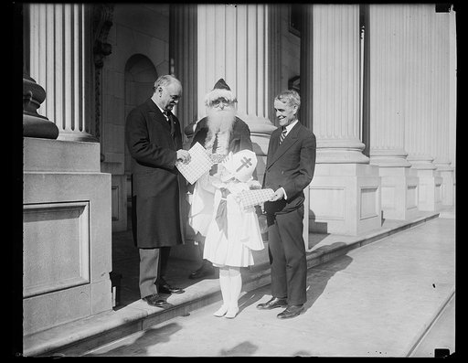 Santa Claus and health crusader call at Capitol to sell Christmas seals. Vice President Curtis and Senator Arthur Capper of Kansas, buying a supply of Tuberculosis Christmas seals from little Nancy Leech, child health crusader, at the Capitol today