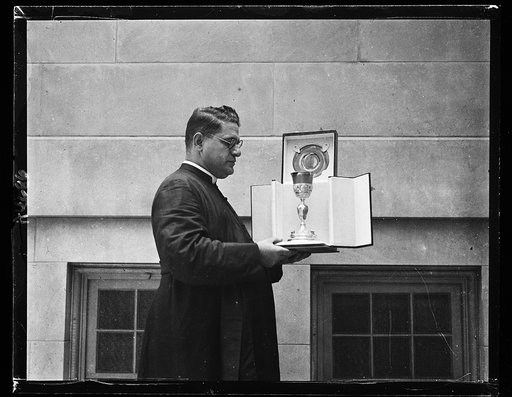 Rev. N. De. Carlo, pastor of Holy Rosary Church, Wash., with a silver chalice presented by King Victor Emmanuel of Italy. The gift is one foot high with reliefs of the apostles cut on the base and delicately engraved handles symbolizing faith, hope, and charity. Presentation made by Dr. Sahetta, cou