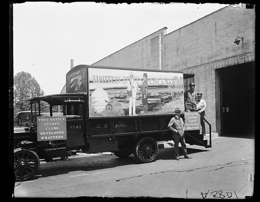 Post office on wheels decorated with Shrine colors. Postmaster Wm. M. Mooney is standing before the office