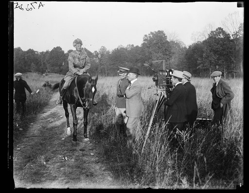 Man dressed on pioneer costume on horse with motion picture film crew