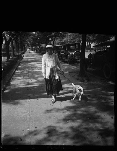 Peter Pan Clark, the small wire-haired terrier puppy and adopted member of the household of Mr. and Mrs. Edw. T. Clark, walking on 16th St., Wash., with Mrs. Clark, wife of the Personal Secy. to Pres. Coolidge. It remained for Peter Pan to be the 1st dog to call at the W.H. [i.e., White House] and l