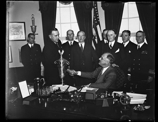 PRESIDENT AWARDS SAFE FLYING TROPHY. WASHINGTON, D.C. PRESIDENT ROOSEVELT, SEATED, AWARDS THE HERBERT SCHIFF TROPHY FOR SAFE FLYING TO LT. PHIL L. HAYNES, COMMANDER OF TRAINING SQUADRON NO. 2 AT THE NAVAL AIR STATION AT PENSACOLA, FLORIDA. T. HAYNES, LEFT, SEC. CLAUDE SWANSON, CENTER, AND SCHIFF STA