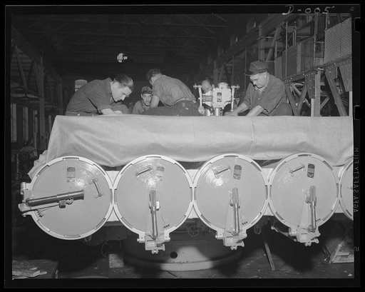 Cooperation on a torpedo tube mount. Skilled workers in an eastern Navy yard arsenal putting the finishing touches on a torpedo tube mount. This arsenal is one of eleven working at top speed for the expanded war program of the Navy