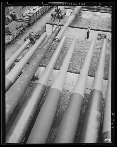 Tons of big guns for the Navy. Getting ready to finish the last of this row of big guns at an eastern Navy yard. The guns have to be shifted by overhead pulleys. This is part of the Navy's war program to provide a two-ocean Navy.