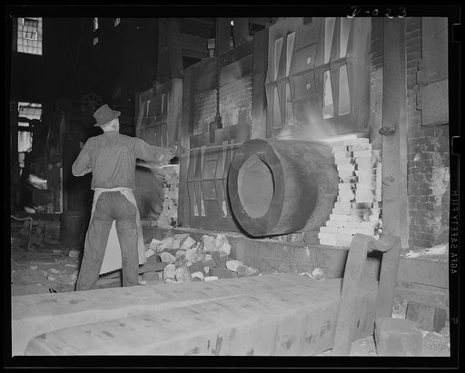 Fitting a round peg in a square hole. Heating the cylinder for a large gun preparatory to forging it. Production of these guns for the war program is going ahead at top speed in eleven Navy arsenals throughout the country