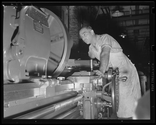 Keeping his eyes on the wheel. Turning an indicator on one of the big machines at a large Army arsenal working around the clock for war needs