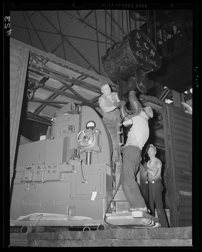 Giving defense a lift. A mighty crane installs one of the big machines in a large eastern arsenal. The apparatus going in is a major capacity cylindrical grinder