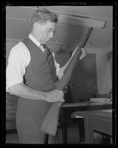 The man behind the gun. John C. Garand, inventor of the semi-automatic rifle now being turned out in large quantities under the war program, looks over one of the guns