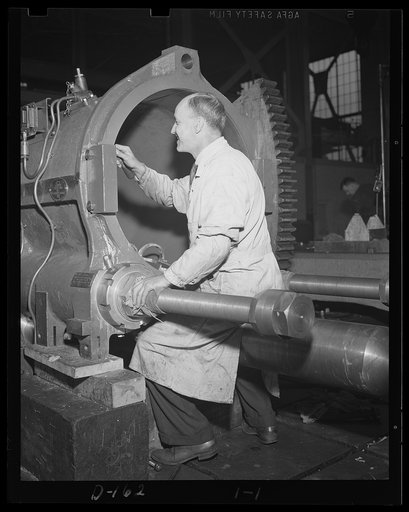 Proud of his job. Smiling worker in an eastern arsenal hand finishes the interior surface of a cradle for an 8-inch gun, railway carriage