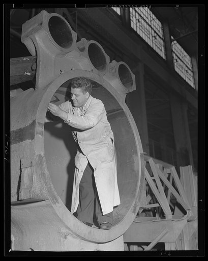 Checking up. The man-sized cradle for a 16-inch gun, barbette carriage, is inspected in an eastern arsenal. This part is destined for one of the big guns required by the war program