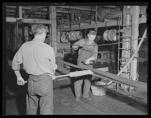 Tending their "tatting." Men at an eastern Navy yard manufacture a boat grippe in the rigging loft of the big government plant now rushing parts and appliances of all kinds for our Navy