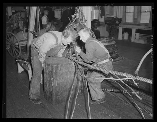 Hold everything. Strain above on a worker's face as he aids his mate to splice wire cable in the rigging loft at an eastern Navy yard. Miles of stout cable are needed for Uncle Sam's fleet