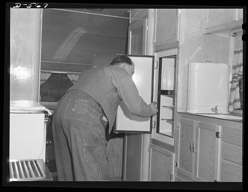 Complete with icebox for raiding. Workman peering into refrigerator in one of a group trailers being used for purpose of temporary housing of defense workers. Note efficient utilization of interior space for cabinets and work surfaces