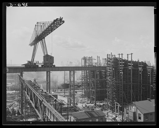 Newport News, Virginia. A small section of the shipyard, showing an overhead travelling ("Gantry") crane in the foreground. There are two ways on which ships are being built visible in the picture. The ship at far background is the S.S. American