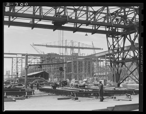 Newport News, Virginia. General shipyard scene, with ships under construction on ways in the background. A stationary overhead crane appears in the foreground of the picture