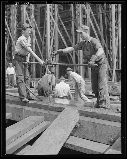 Newport News, Virginia. Workmen removing bolts from the ways after a ship has been launched. The grease on the ways can still be seen