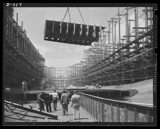 Newport News, Virginia. Placing a floor section in a C-3. Several floor sections, already installed, can be seen in the foreground. Workmen are standing in what will be the lowest part of the hold of the ship, near the keel