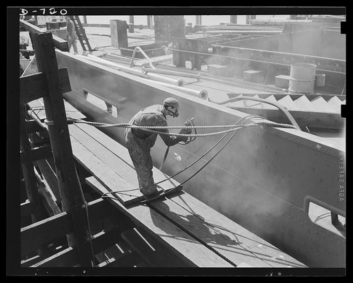 Newport News, Virginia. Spray painting the outside of the hull of a C-3. The section the worker is painting here is known technically as a deck thwart